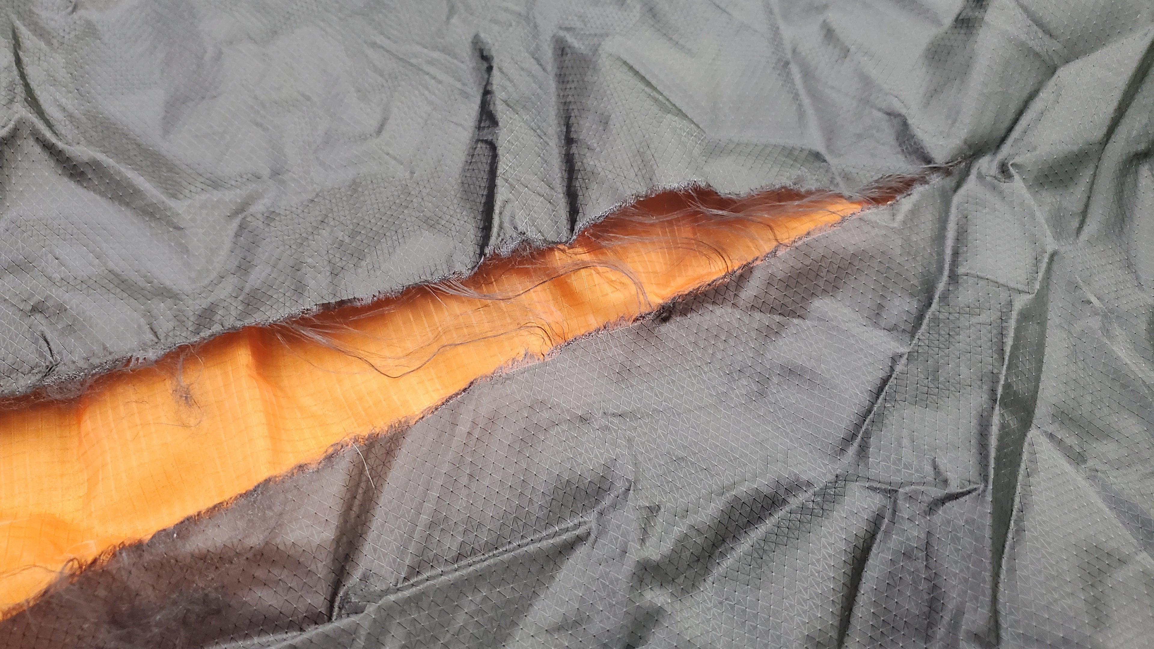 Damaged camping hammock made from ultralight nylon fabrics - 1.2oz ultralight Mtn-XL fabric black, and 1.0oz ultralight monolite mesh in burnt orange