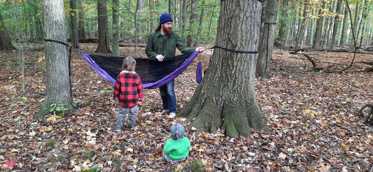 adult and a child setting up a hammock in a forest.